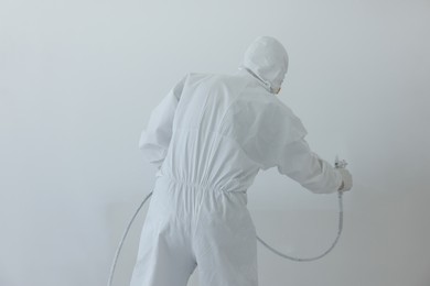 Photo of Decorator painting wall with spray, back view