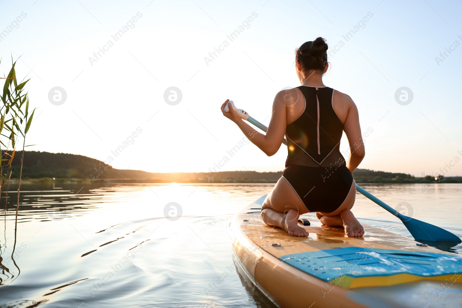 Photo of Woman paddle boarding on SUP board in river at sunset, back view