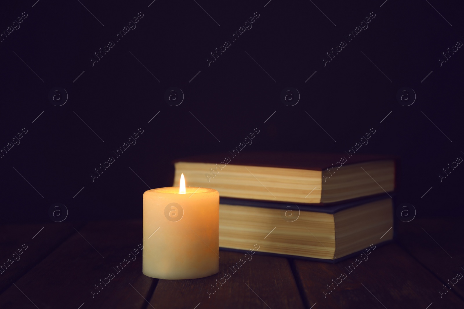 Photo of Burning candles and stack of books on wooden table in darkness