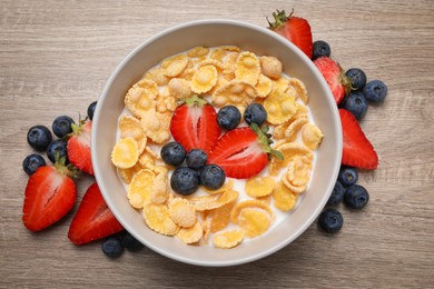 Delicious crispy cornflakes with milk and fresh berries on wooden table, flat lay