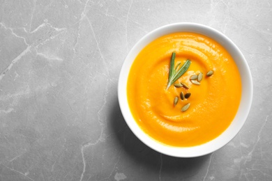 Photo of Bowl of tasty pumpkin soup and space for text on gray table, top view