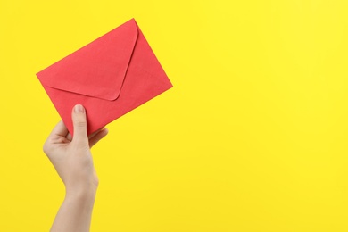 Woman holding red paper envelope on yellow background, closeup. Space for text