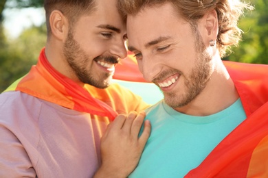 Photo of Happy gay couple with rainbow flag outdoors