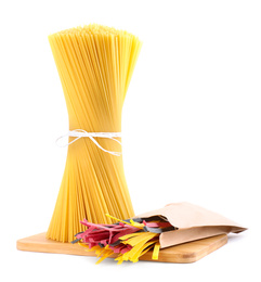 Photo of Wooden board with spaghetti and colorful tagliatelle pasta isolated on white