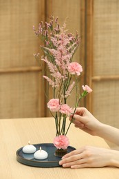 Woman creating stylish ikebana with beautiful pink flowers at table, closeup