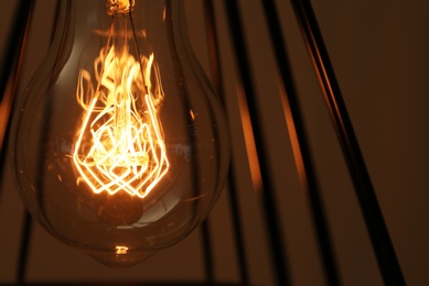 Hanging lamp bulb in chandelier against brown background, closeup