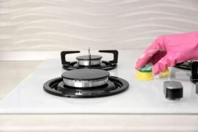 Photo of Person cleaning gas stove with sponge, closeup