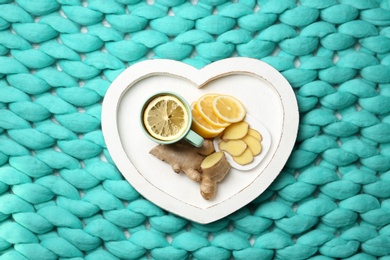 Photo of Heart shaped tray with lemon ginger tea on knitted background, flat lay