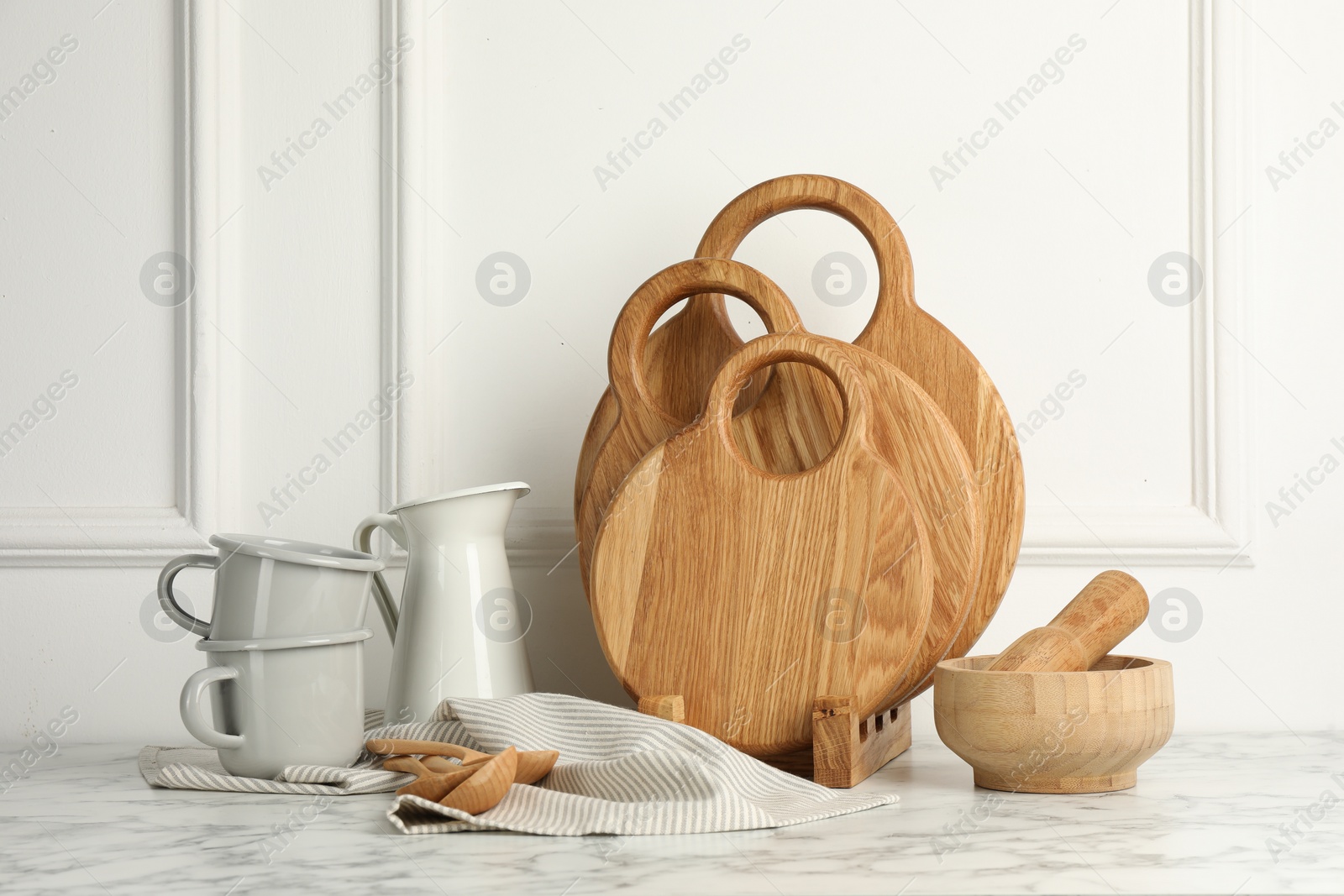 Photo of Wooden cutting boards, spoons and dishware on white marble table