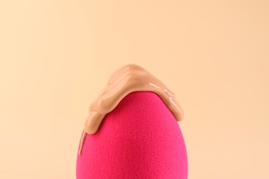 Photo of Pink makeup sponge with skin foundation on beige background, closeup