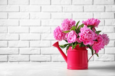 Photo of Watering can with beautiful peony flowers on table against brick wall