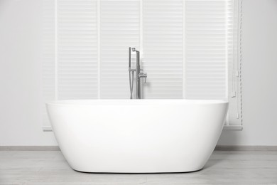 Stylish ceramic tub near window with blinds indoors