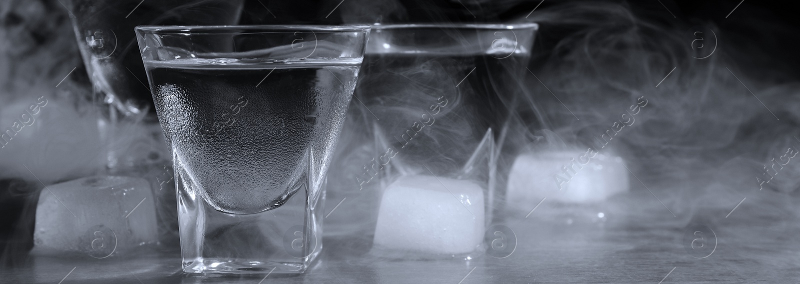 Image of Vodka in shot glasses with ice on table against black background, closeup. Banner design