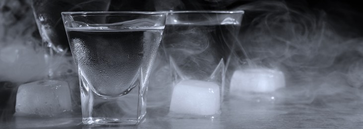 Vodka in shot glasses with ice on table against black background, closeup. Banner design