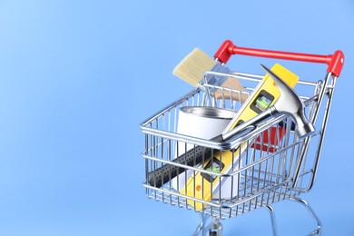 Photo of Small shopping cart with paint and renovation equipment on light blue background. Space for text