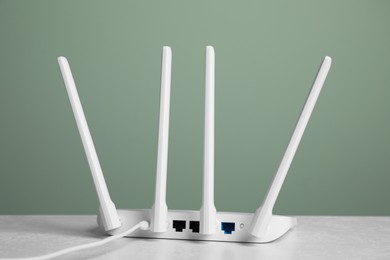 Photo of New modern Wi-Fi router on white table near green wall