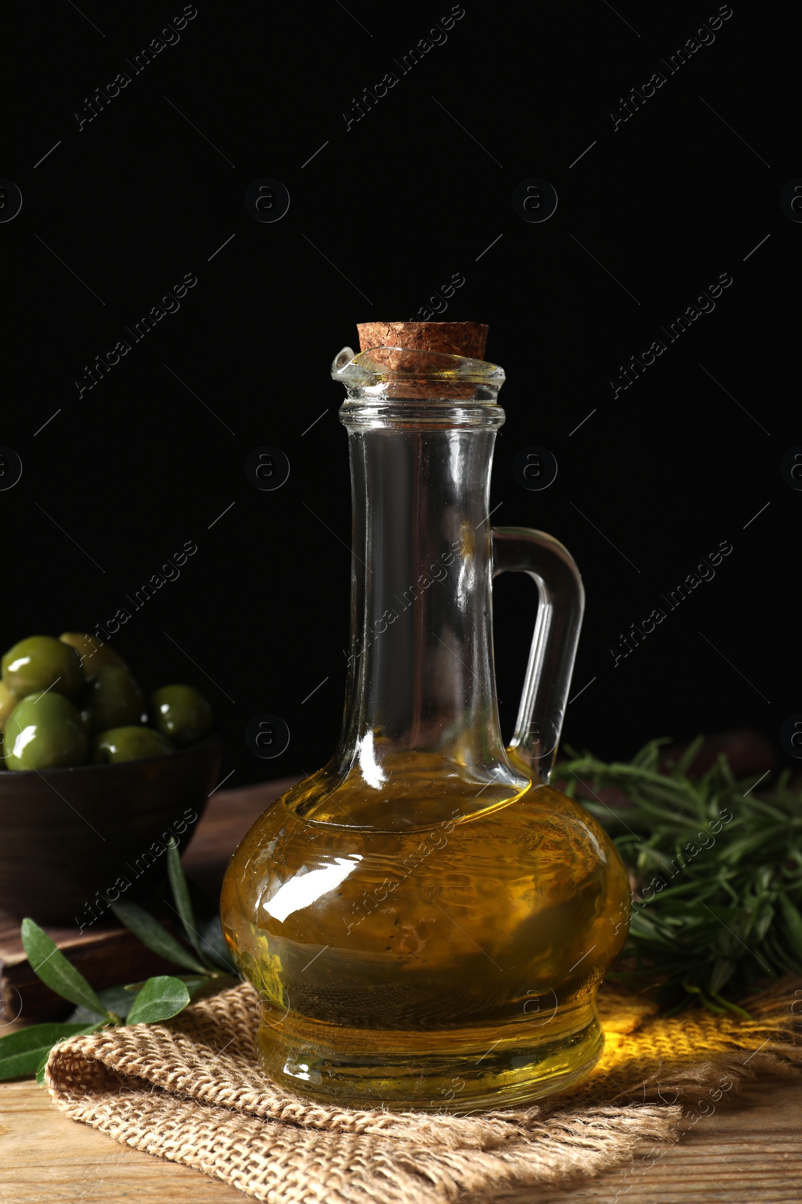 Photo of Glass jug of oil, ripe olives and green leaves on wooden table