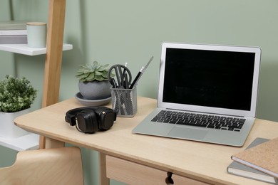 Photo of Workplace with laptop and stationery on desk near green wall. Home office