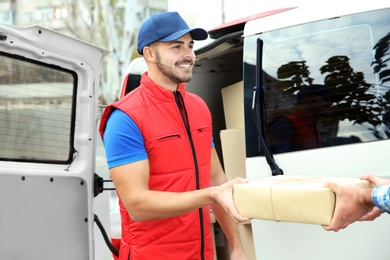 Photo of Young courier giving parcel to customer outdoors