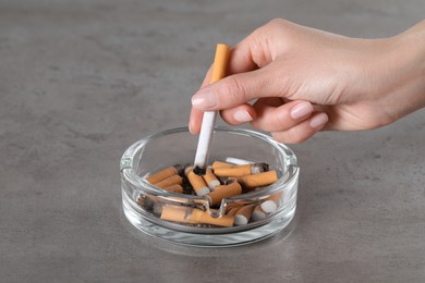 Photo of Woman putting out cigarette in ashtray on grey table, closeup