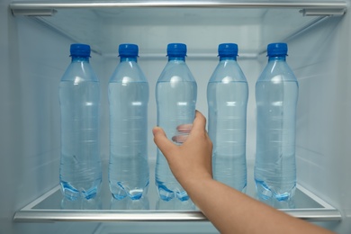 Photo of Woman taking bottle of fresh water from fridge shelf, closeup