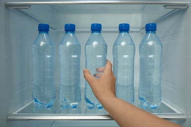 Woman taking bottle of fresh water from fridge shelf, closeup