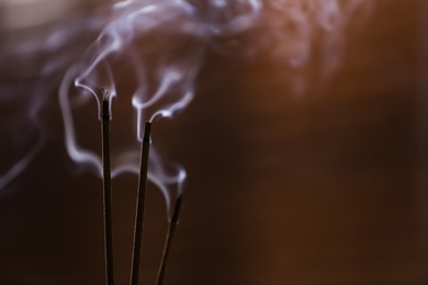 Photo of Incense sticks smoldering on blurred background, closeup. Space for text