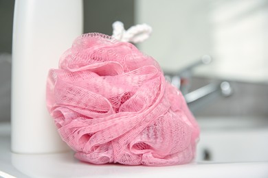 Photo of Pink sponge and shower gel bottle on washbasin in bathroom, closeup