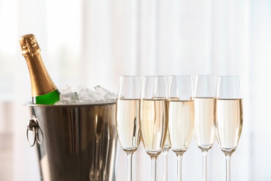 Photo of Glasses with champagne and bottle in bucket against blurred background