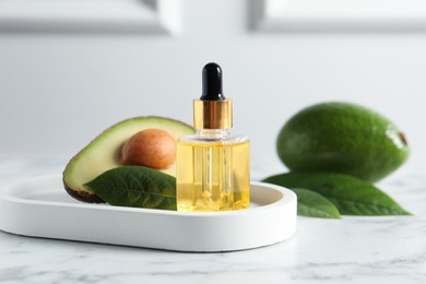 Bottle of essential oil and avocados on white marble table
