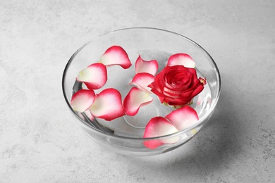 Photo of Glass bowl with aroma spa water, rose and petals on grey background