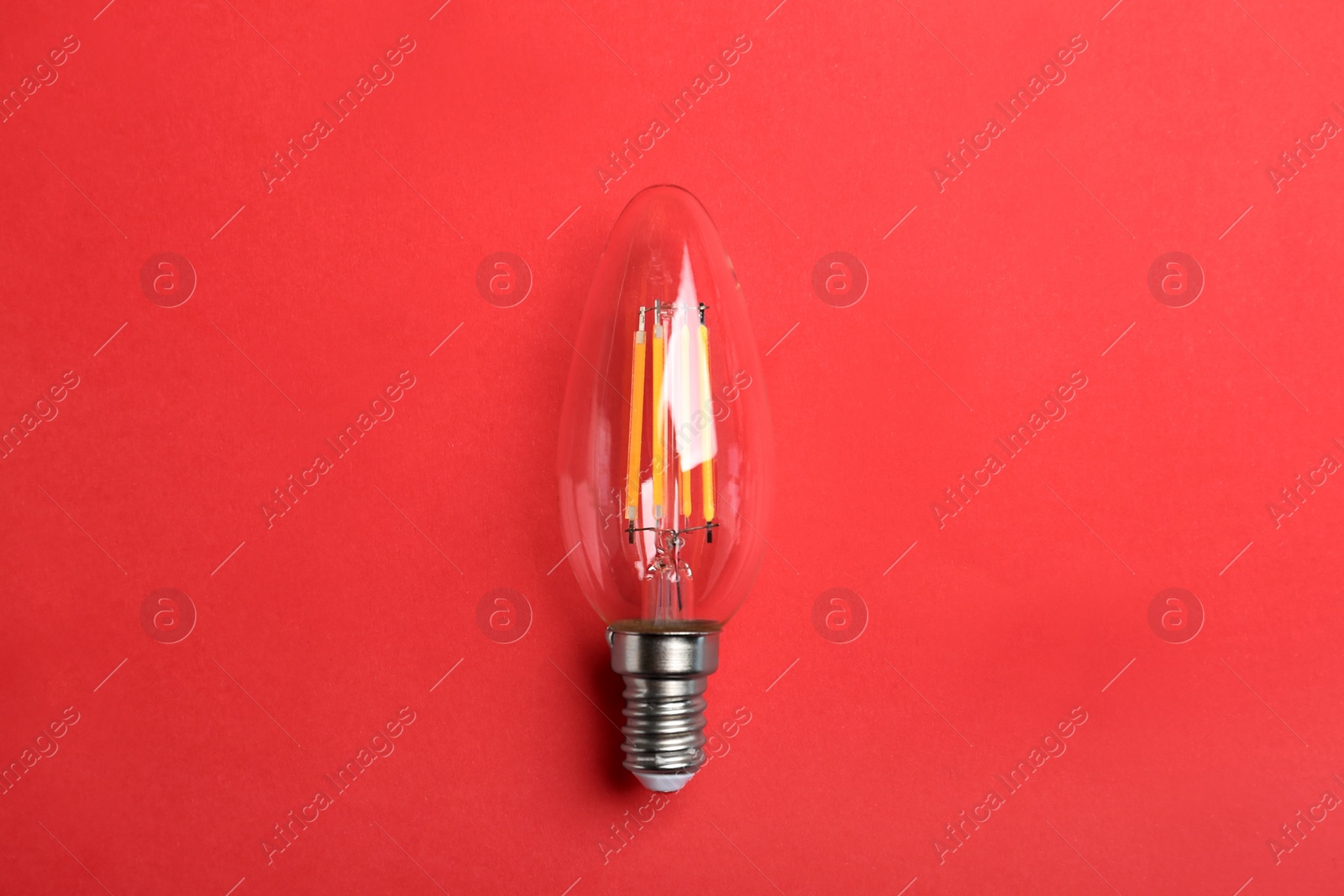 Photo of Vintage filament lamp bulb on red background, top view