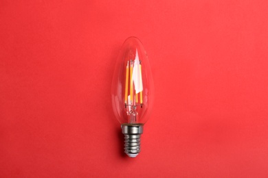 Vintage filament lamp bulb on red background, top view