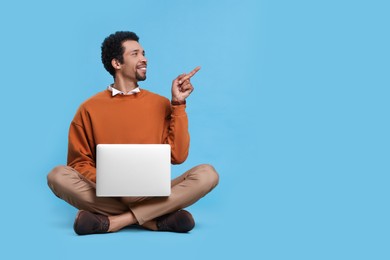 Photo of Handsome man with laptop pointing at something on light blue background. Space for text