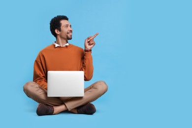 Handsome man with laptop pointing at something on light blue background. Space for text