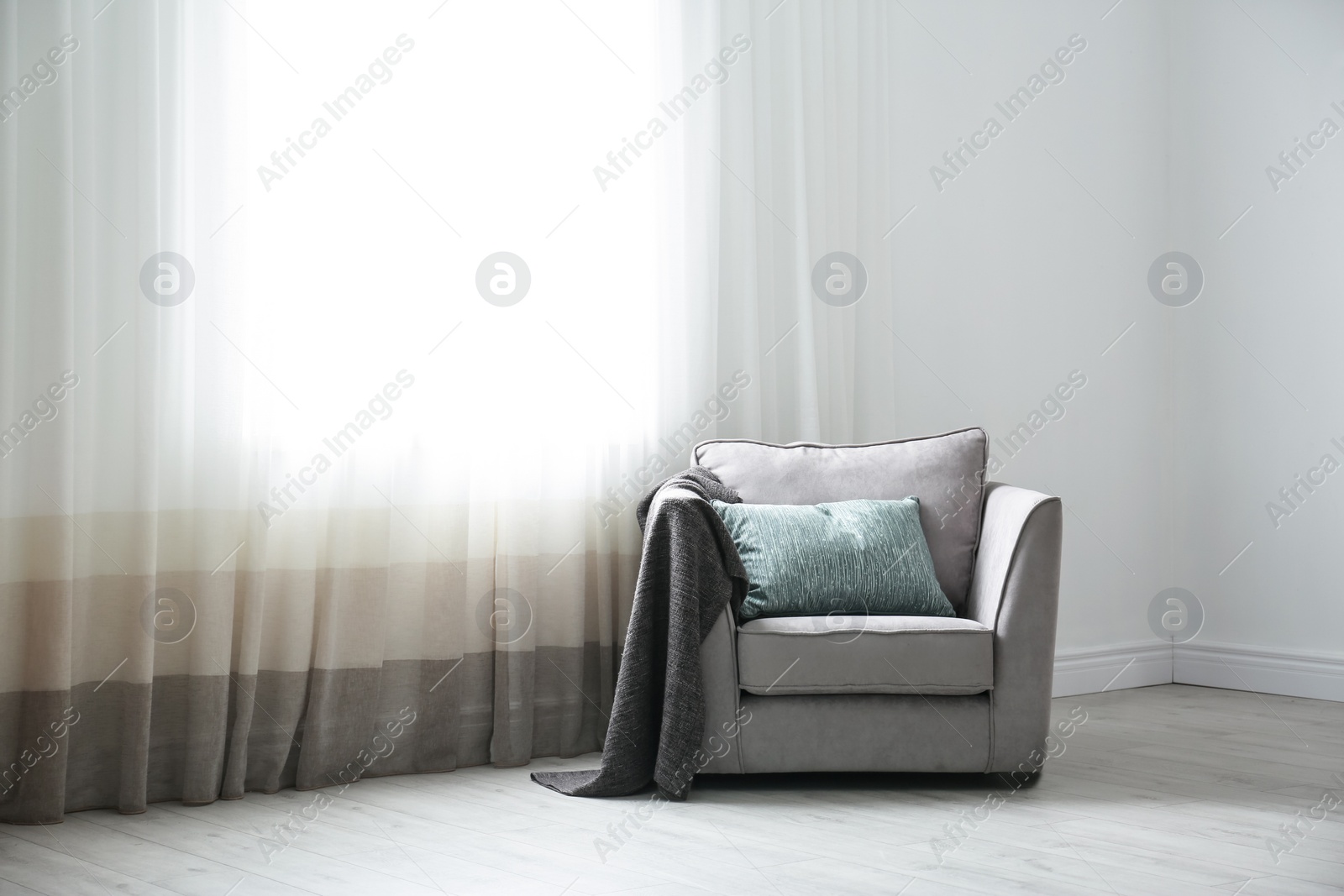 Photo of Cozy armchair with pillows and plaid near window in room. Interior design