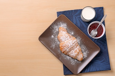Plate with tasty croissant, glass of milk and jam on wooden background, top view
