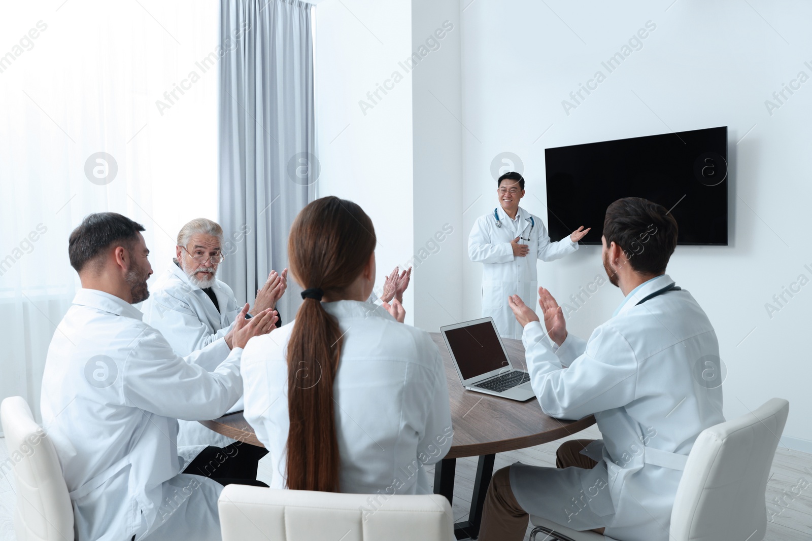 Photo of Team of doctors listening to speaker report near tv screen in meeting room. Medical conference