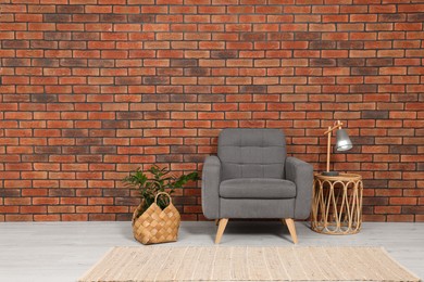 Stylish room interior with armchair and plant near brick wall, space for text