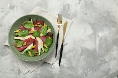 Photo of Delicious bresaola salad in bowl served on light grey textured table, flat lay. Space for text