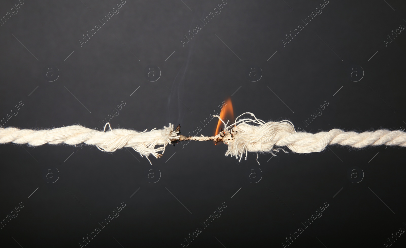 Photo of Burning frayed rope at breaking point on gray background