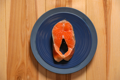 Photo of Fresh raw fish steak on wooden table, top view
