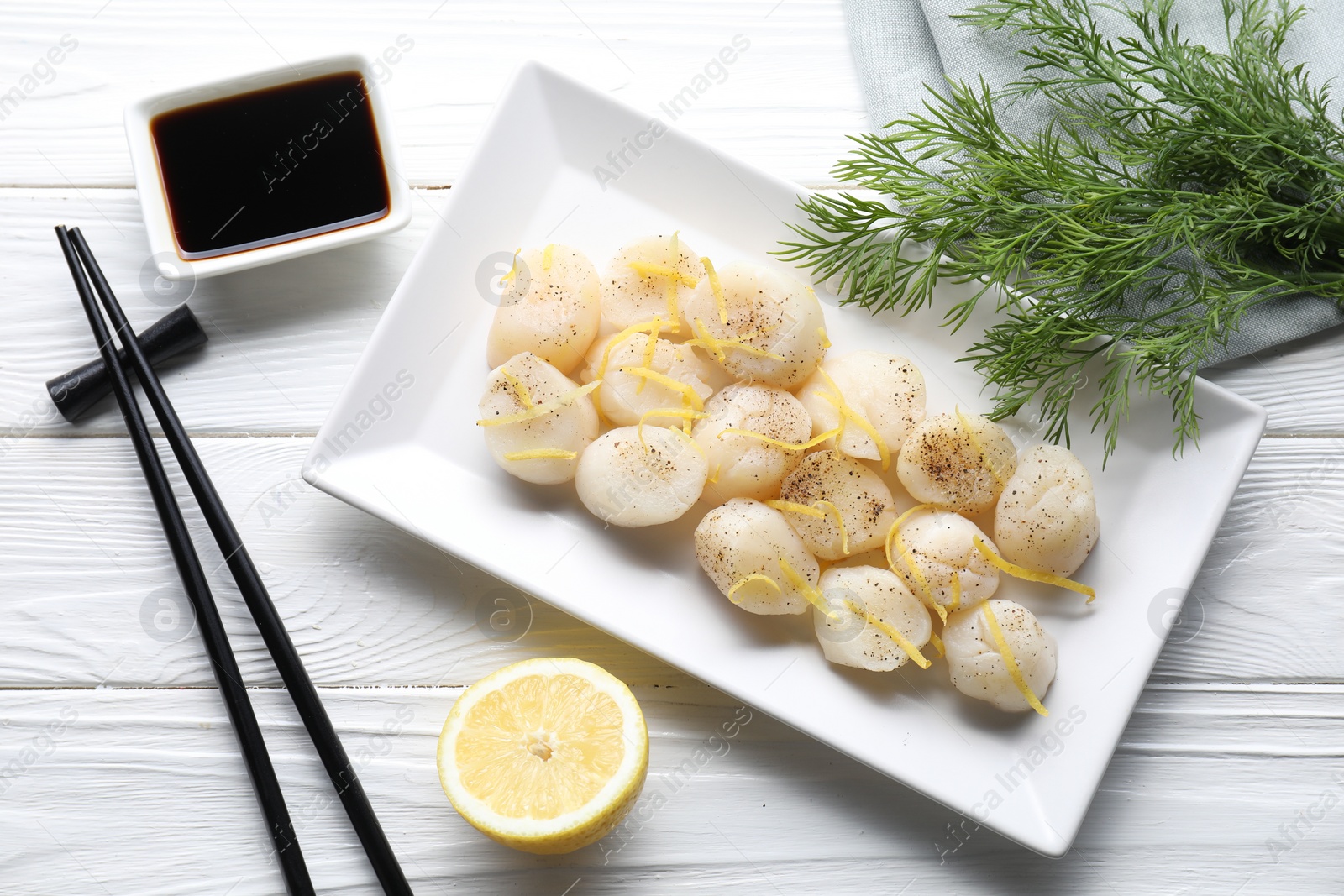 Photo of Raw scallops with milled pepper, lemon zest, dill and soy sauce on white wooden table, flat lay