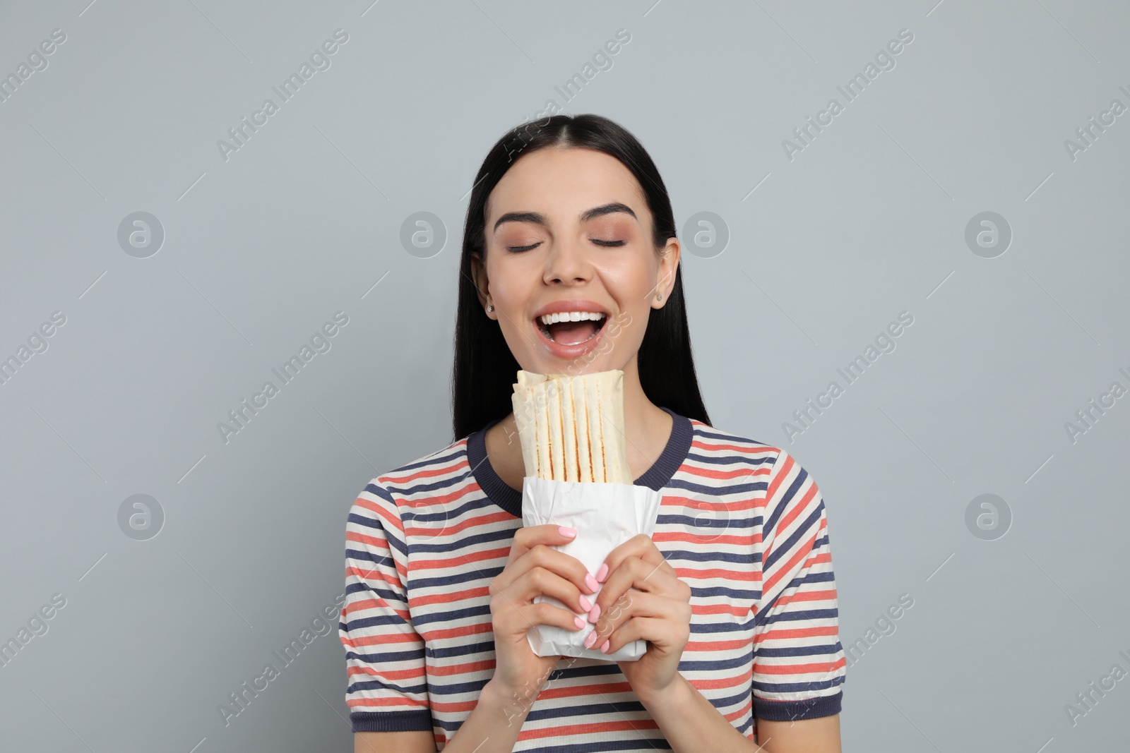 Photo of Young woman eating delicious shawarma on grey background