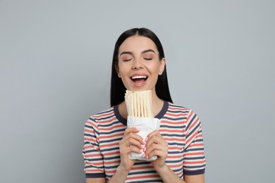 Photo of Young woman eating delicious shawarma on grey background