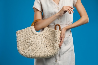 Photo of Young woman with stylish straw bag on blue background, closeup