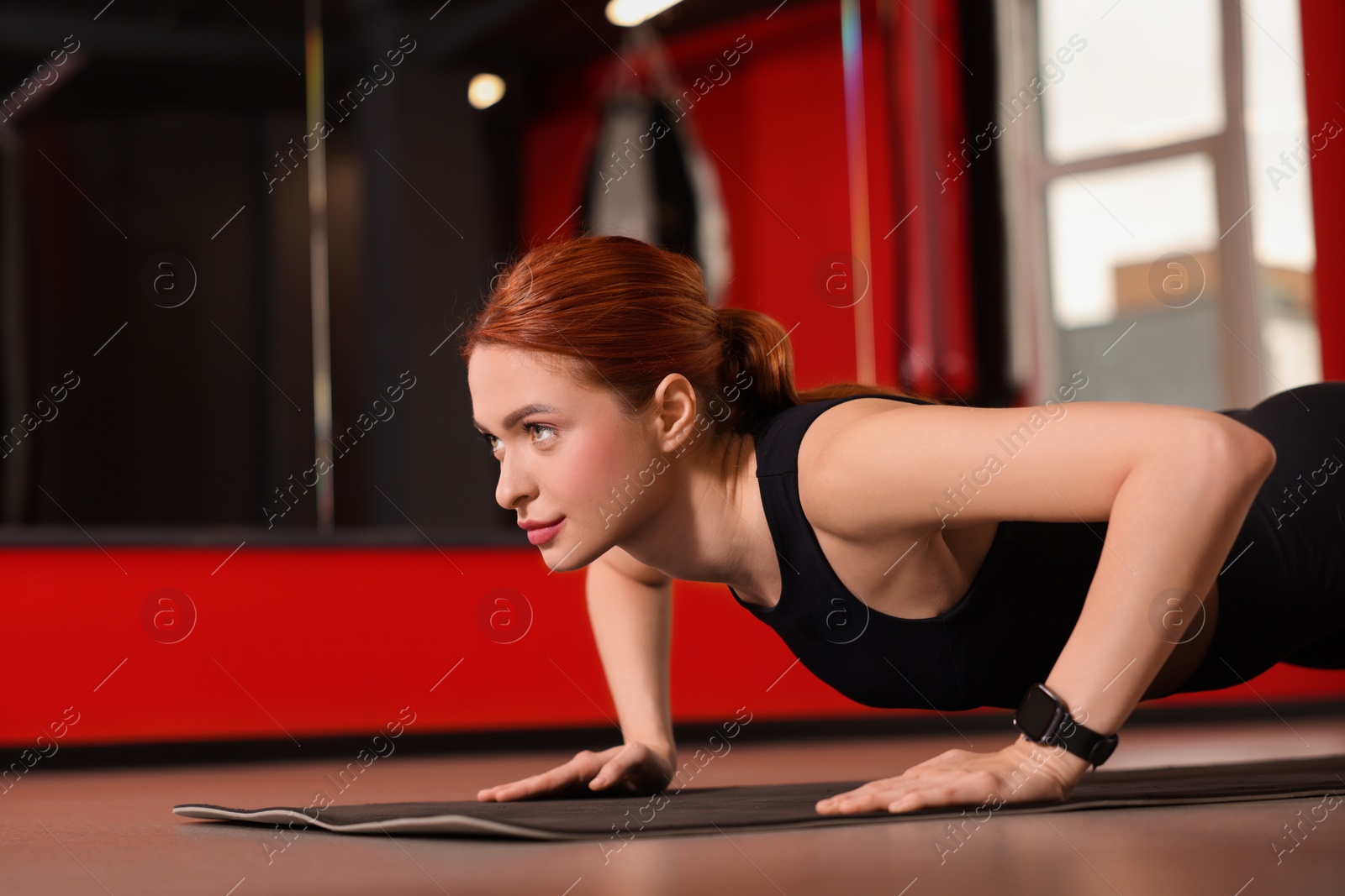 Photo of Athletic young woman doing push ups on mat in gym, space for text