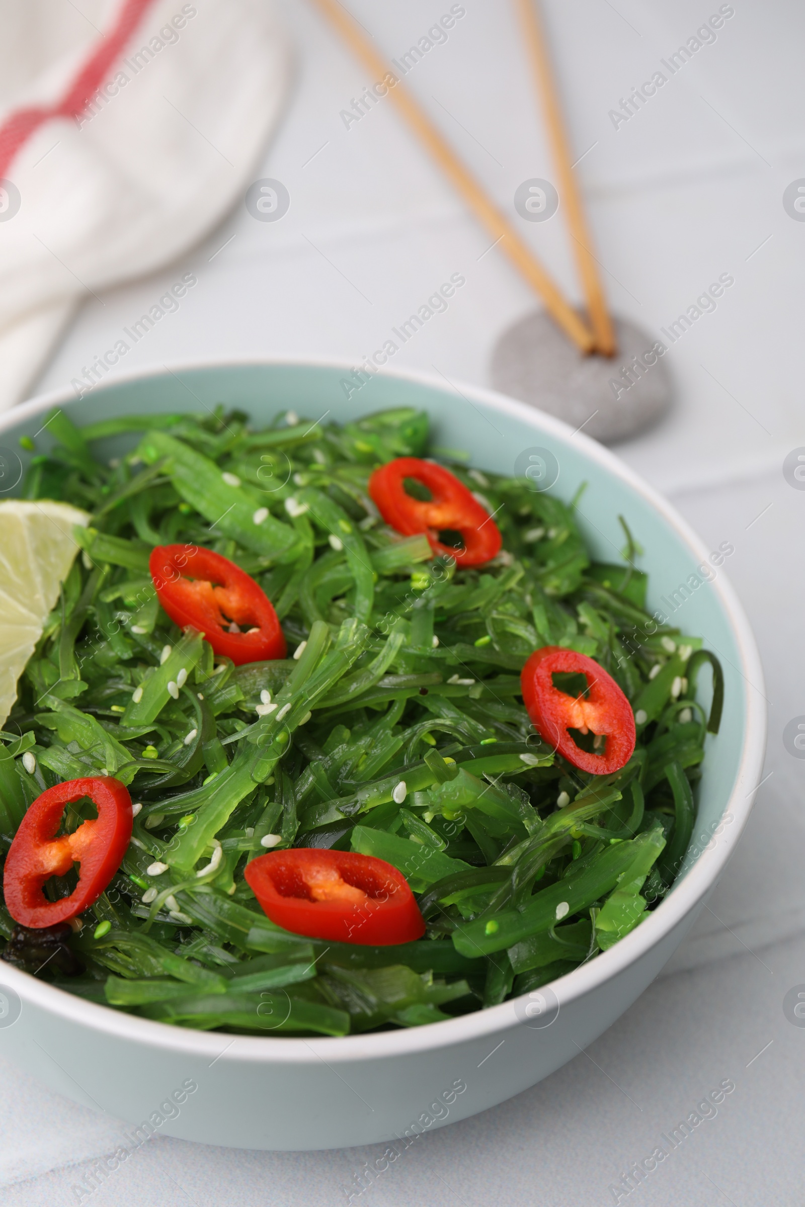 Photo of Tasty seaweed salad in bowl served on white table, closeup