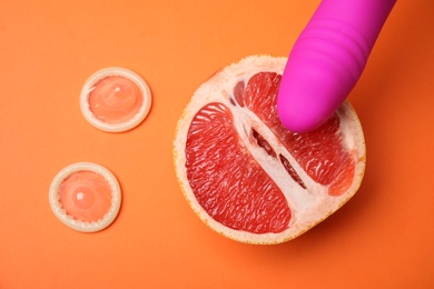 Half of grapefruit, purple vibrator and condoms on orange background, flat lay. Sex concept