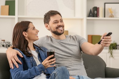 Photo of Happy couple spending time together at home. Man changing TV channels with remote control